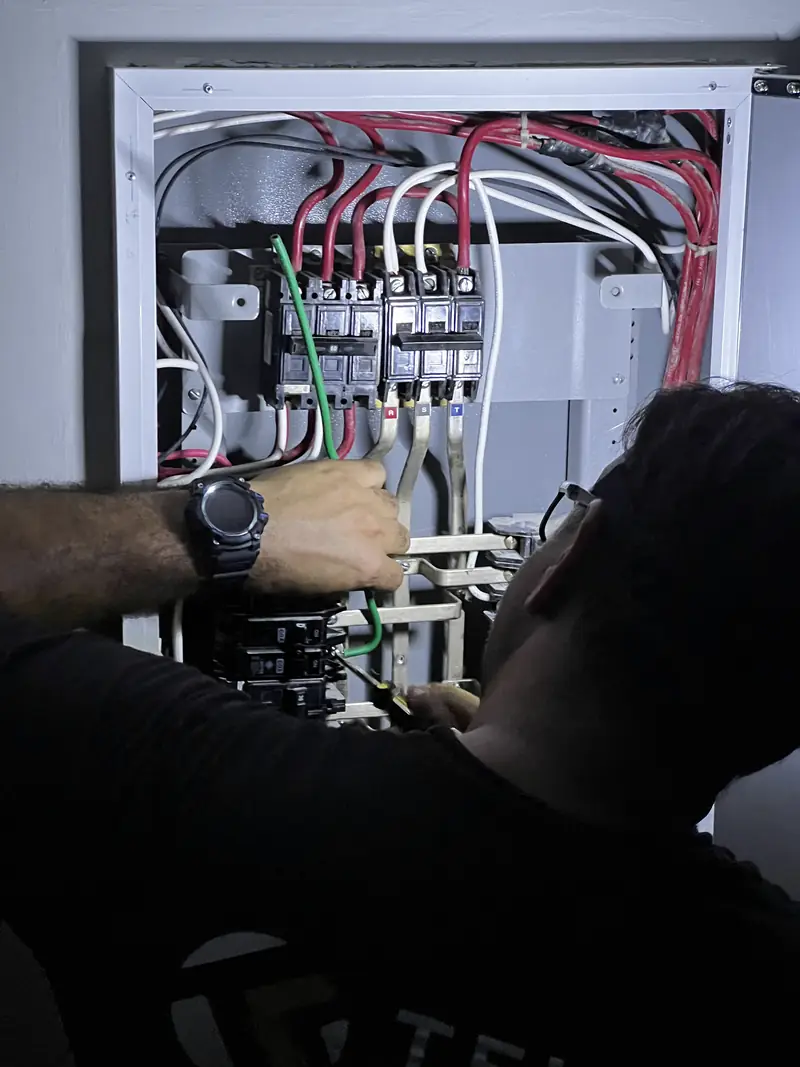 Técnico de Telcom trabajando en un tablero eléctrico, alumbrado con linterna
